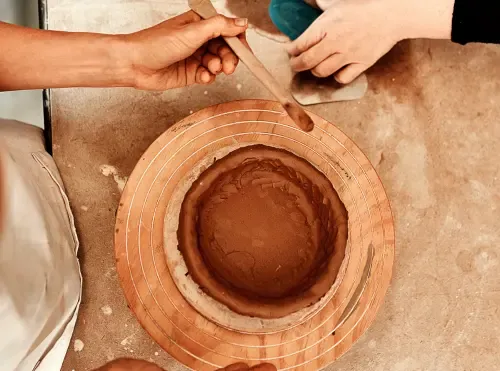 Due persone modellano insieme un vaso di argilla al tornio: l'apprendimento del mestiere accanto a chi sa già farlo.