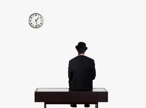 Persona seduta su una panca, vista di spalle, indossa un cappello a bombetta e un abito scuro; sullo sfondo bianco, in alto a sinistra, è appeso un orologio.