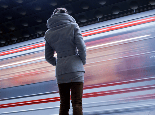 Persona di spalle in attesa - su una banchina della metropilotana - mentre passa un treno ad alta velocità.