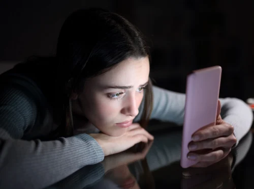 Adolescente sola guarda lo smartphone con espressione preoccupata, simbolo della ricerca di supporto emotivo digitale.
