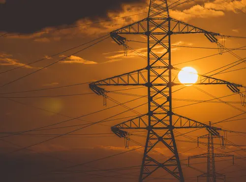 Tralicci dell'alta tensione in controluce al tramonto, con il sole tra i cavi elettrici