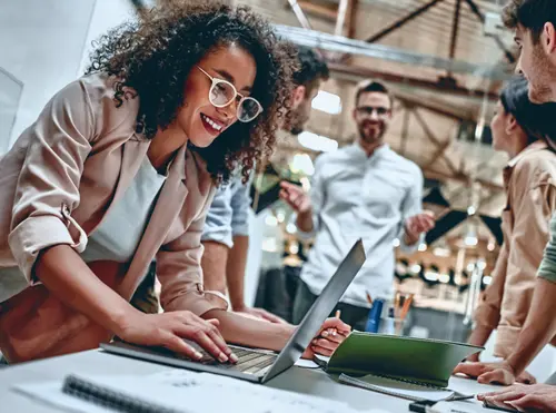 Tre giovani professionisti sorridenti collaborano davanti a un laptop in un ufficio moderno e luminoso