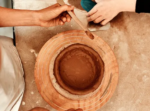 Due persone modellano insieme un vaso di argilla al tornio: l'apprendimento del mestiere accanto a chi sa già farlo.
